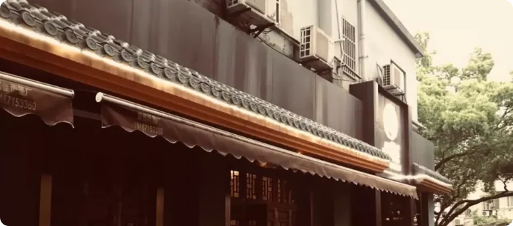杭州巷子里的一家私房菜馆，灰瓦屋檐搭配深色遮阳棚，临街门面颇具烟火气