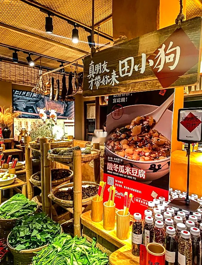 田小狗的明档食材台：竹编吊顶配黑色轨道射灯，灯只落在食材上，竹筐里是干货，上方吊着熏腊，下方一排有机调料瓶，竹筒里插着写菜名的竹签