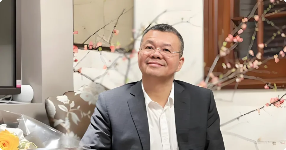 张新民先生坐于花枝掩映的厅堂前，西装白衬衫，神态儒雅